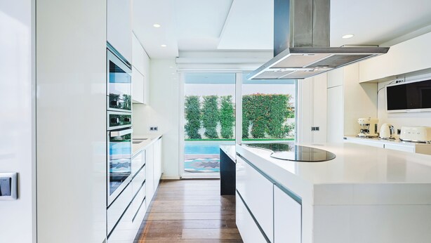 A modern kitchen with white cabinetry, a large island, and a view of a swimming pool.