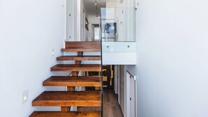 A modern interior with a wooden staircase, a glass railing, and a hallway leading to a door.