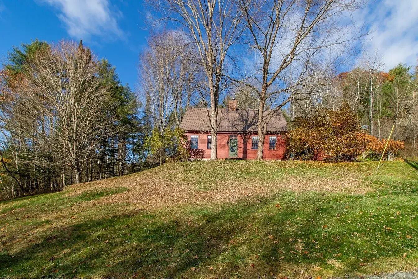 A red brick house with a sloped roof, surrounded by trees and a grassy hill.