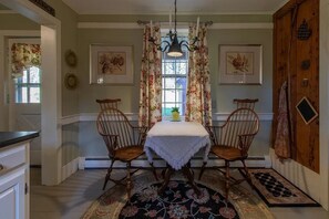A dining area with a table, two chairs, a chandelier, and floral curtains. - Beautiful peaceful country home on 18 acres built 1800 (Ryegate)
