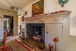 A traditional fireplace with a mantel decorated with fruits and berries, a rustic wooden chair, and a red candle holder. - Beautiful peaceful country home on 18 acres built 1800 (Ryegate)