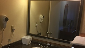 A bathroom with a sink, mirror, hair dryer, and a towel dispenser. - Days Inn by Wyndham Victorville/hesperia I-15 & P (Victorville)