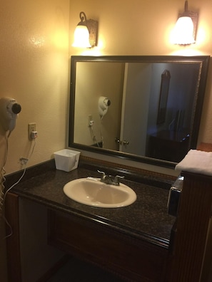 A bathroom with a sink, mirror, hair dryer, and a towel dispenser.