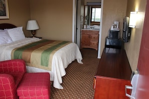 A hotel room with a bed, a desk, a chair, a lamp, a coffee maker, and a mirror.