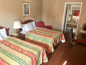 A hotel room with two beds, a desk, a chair, a lamp, and a painting on the wall.