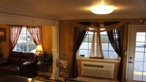 A hotel lobby with a leather sofa, a desk with a computer, a window with curtains, and a door with a sign. - Park Avenue Inn And Suites (Victorville)