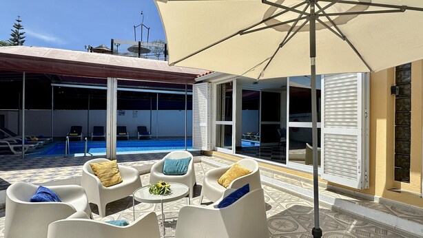 An outdoor seating area with a pool, lounge chairs, and a large umbrella. - Yellow | Private pool | 12 Pax | Albufeira (Albufeira)