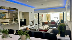 A modern living room with a flat-screen TV, a fireplace, a dining area with a table and chairs, and a kitchen area with a refrigerator and a microwave. - Yellow | Private pool | 12 Pax | Albufeira (Albufeira)