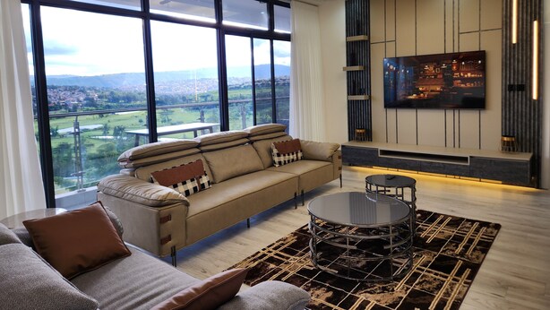 Ein modernes Wohnzimmer mit großem Fenster, einer Couch, einem Couchtisch und einem an der Wand befestigten Fernseher.