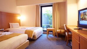Hotellihuone, jossa on kaksi sänkyä, työpöytä, tuoli, televisio ja ikkuna, jossa on verhot.