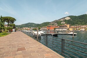Eine Uferpromenade mit Pflasterweg, Booten im Yachthafen und Gebäuden im traditionellen Baustil im Hintergrund.