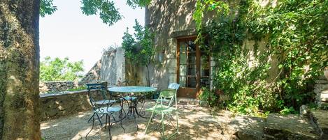 An outdoor seating area with a table and chairs, surrounded by stone walls and greenery.