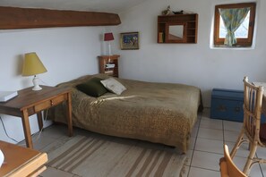 A bedroom with a bed, a desk, a chair, a lamp, a bookshelf, a window, and a small cabinet.