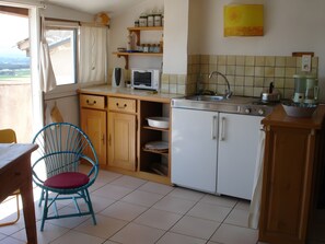 A kitchen with wooden cabinets, a microwave, a sink, and a dining area with a chair.