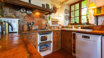 A rustic kitchen with a wooden countertop, a built-in oven, a dishwasher, and a window with a view of greenery.