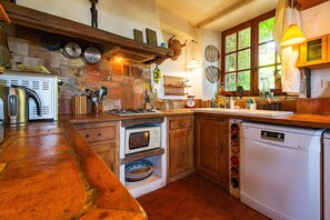 A rustic kitchen with a wooden countertop, a built-in oven, a dishwasher, and a window with a view of greenery.