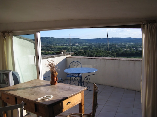 A balcony with a table, chairs, and a view of distant hills.