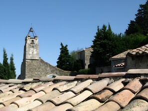 A stone building with a bell tower, surrounded by trees and a tiled roof.