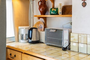A kitchenette with a coffee maker, kettle, and a portable heater.