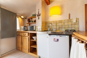 A compact kitchen with a refrigerator, sink, and a small dishwasher. There are wooden cabinets and a shelf with kitchen items.