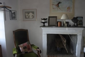 A room with a fireplace, a green armchair, and various framed artworks on the wall.