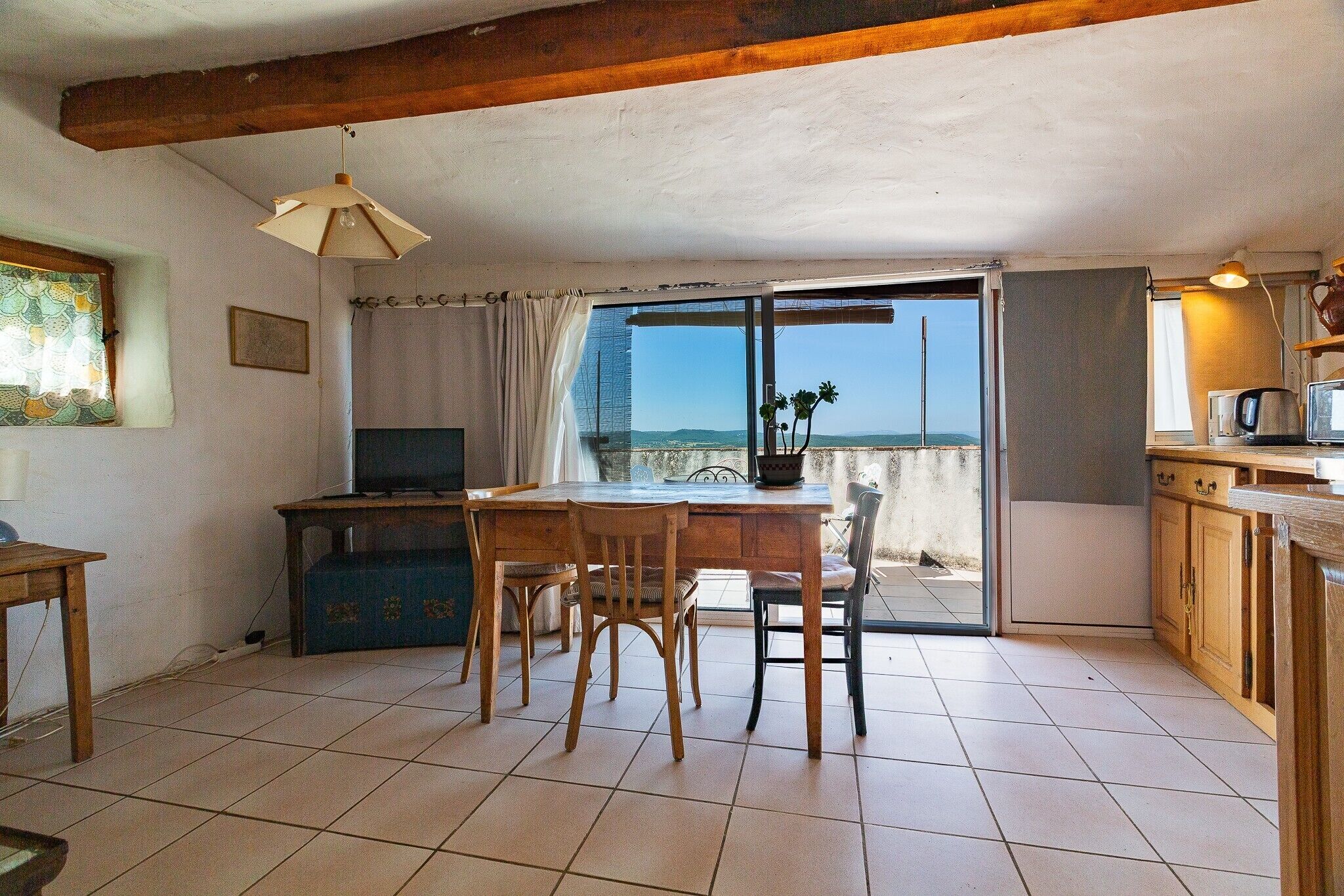 A kitchen with a dining table, chairs, a TV, and a view through a glass door.
