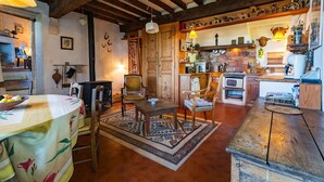 Un intérieur rustique avec une table à manger en bois, des chaises, un canapé et un coin cuisine équipé d’appareils électroménagers.