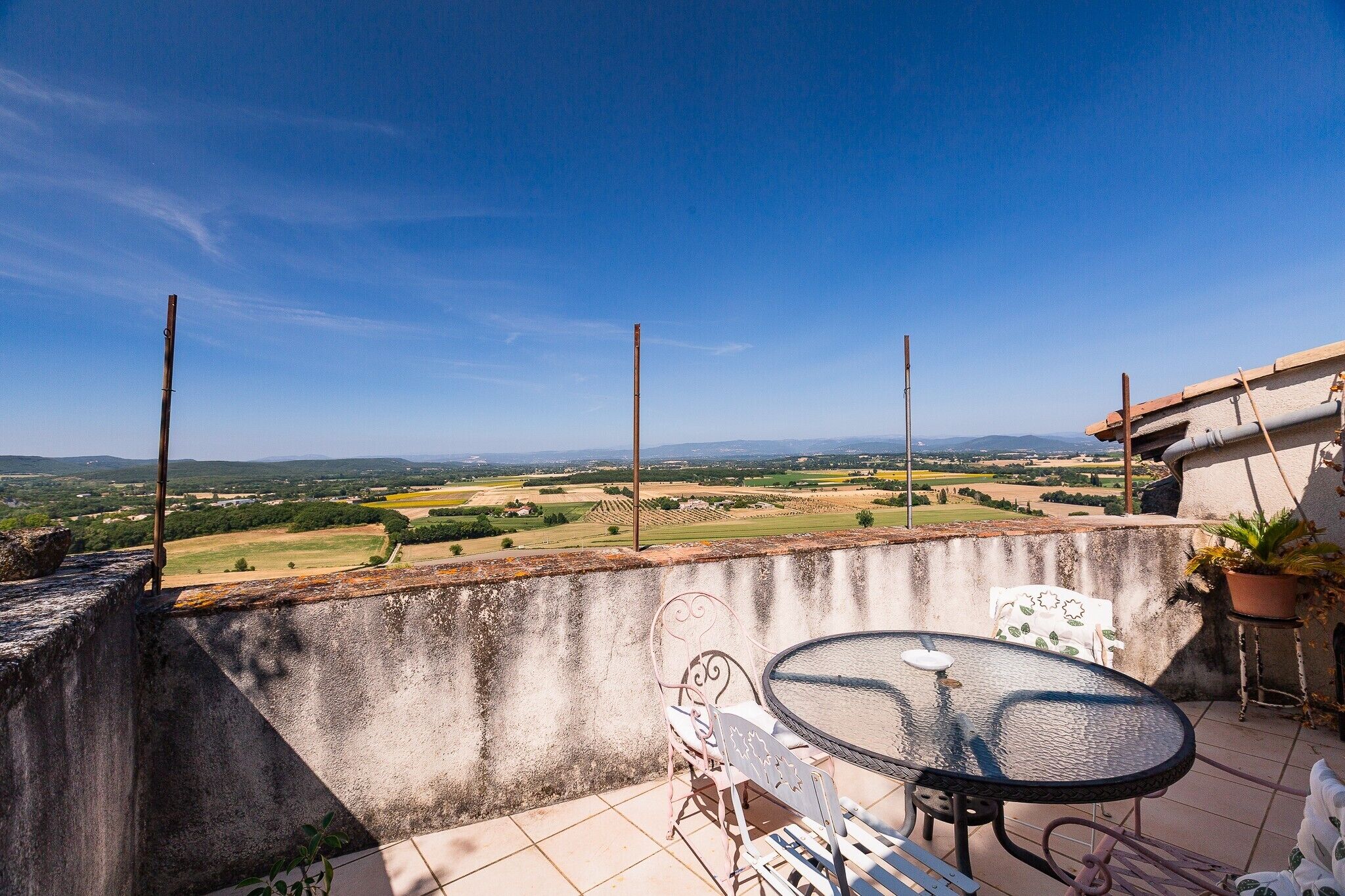 A terrace with a table and chairs, overlooking a rural landscape with fields and distant mountains.