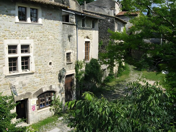 A stone building with multiple windows and a narrow pathway leading to the entrance. - 'Du Bas' Apartment with Mountain View, Private Garden and Wi-Fi (La Bégude-de-Mazenc)