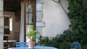Ein blaues Metall-Tisch- und Stuhlgarnitur steht vor einem Gebäude mit einer Steinmauer. Auf dem Tisch steht ein Blumentopf.