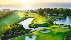 Ein Golfplatz mit Wasserhindernissen, umgeben von Bäumen und Gebäuden.