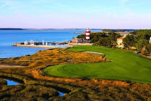 Un campo de golf frente al mar con un faro, un puerto deportivo y una casa club.