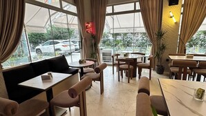A restaurant with a modern interior, featuring a mix of seating arrangements including a sofa and tables, large windows with curtains, and a neon sign. - Port Hotel (Istanbul)