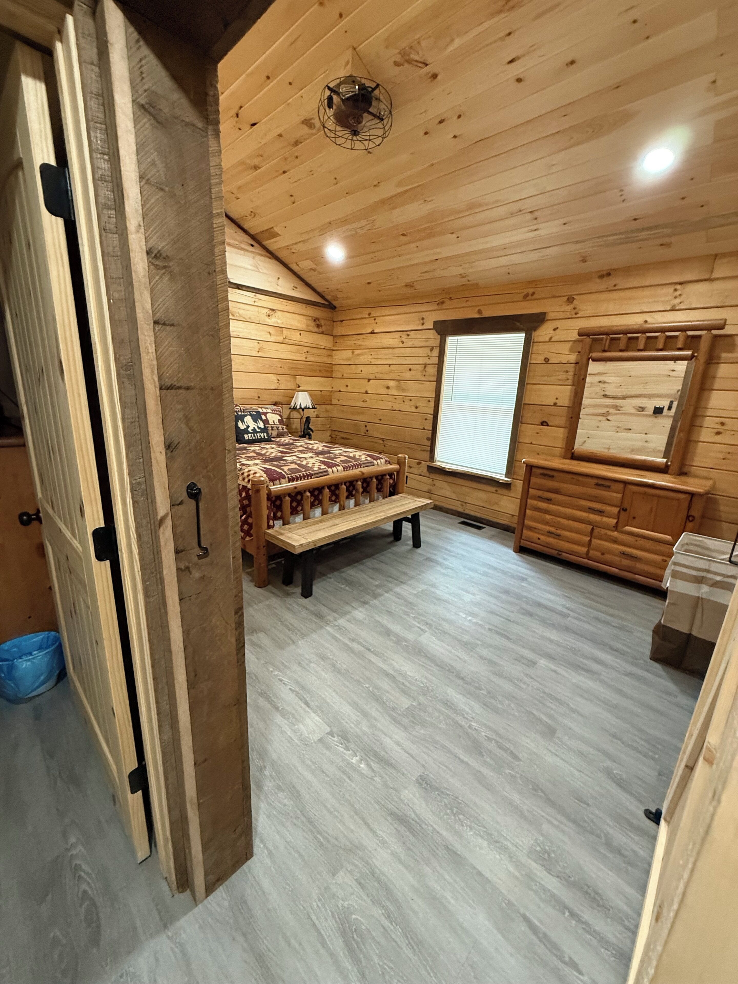 L’intérieur d’un chalet en bois, avec un lit, un banc, une fenêtre et un miroir.