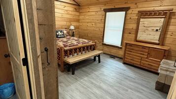 L’intérieur d’un chalet en bois, avec un lit, un banc, une fenêtre et un miroir.