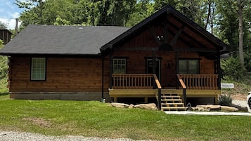 Une cabane en bois dotée d’un porche, d’une petite entrée et d’un panneau indiquant qu’il s’agit d’un terrain de camping situé en montagne.