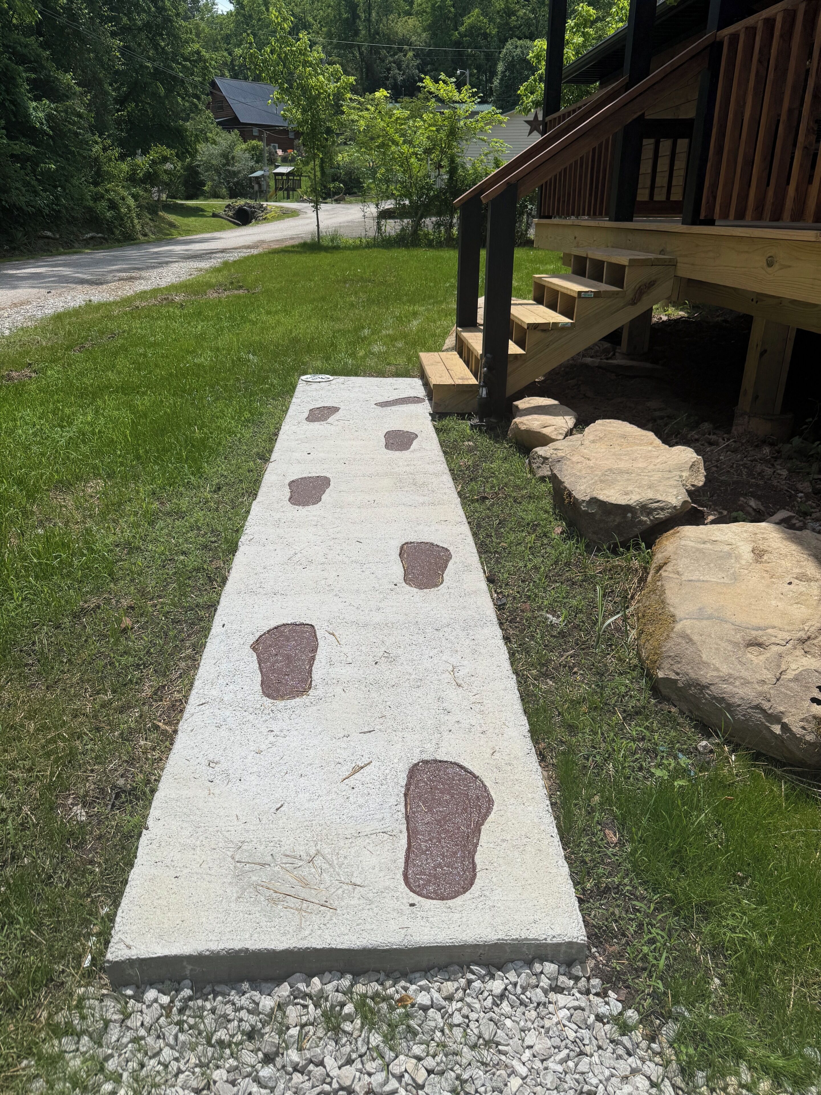 A concrete path with footprints leading to a wooden deck with a staircase.