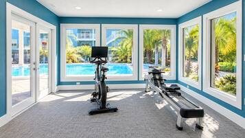 A gym with exercise equipment and large windows overlooking a pool area.