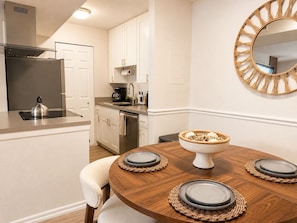 A modern kitchen with a built-in stove, a refrigerator, and a dining area with a wooden table set for four. - South Tampa Retreat | Near Airport & Downtown (Tampa)