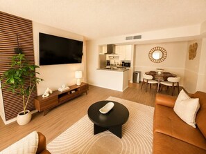 A modern living room with a flat-screen TV, a dining area, and a kitchen in the background. - Stylish Tampa Getaway | Airport, Stadiums & Beaches (Tampa)