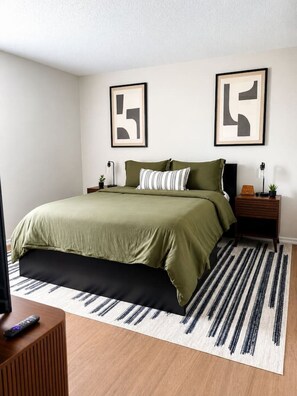 A bedroom with a bed, two nightstands, a TV stand, and abstract wall art. - South Tampa Retreat | Near Airport & Downtown (Tampa)