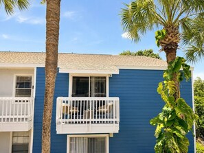 A two-story building with a blue exterior, a balcony with wicker furniture, and a palm tree in the foreground. - South Tampa Retreat | Near Airport & Downtown (Tampa)