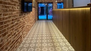 A hallway with brick walls, patterned flooring, a ceiling light fixture, and a flat-screen TV mounted on the wall. - Santra Bosphorus Pansiyon (Istanbul)