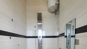 Un bagno con pareti rivestite di piastrelle bianche, una fascia decorativa a righe bianche e nere, una doccia con pannello comandi, un lavandino con specchio e un porta asciugamani.