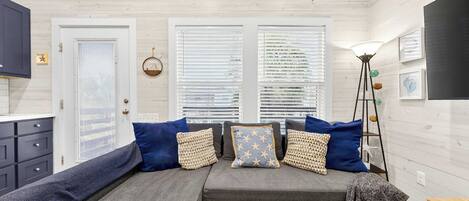 A cozy room with a sofa set, a floor lamp, and a view through the windows.