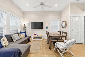 A living room with a sofa, TV, dining table, chairs, and a ceiling fan. - Coastal Command | Beach Bungalow | 11th st (Port Aransas)