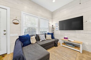 Sala de estar com sofá seccional, televisão de tela plana e piso de madeira.