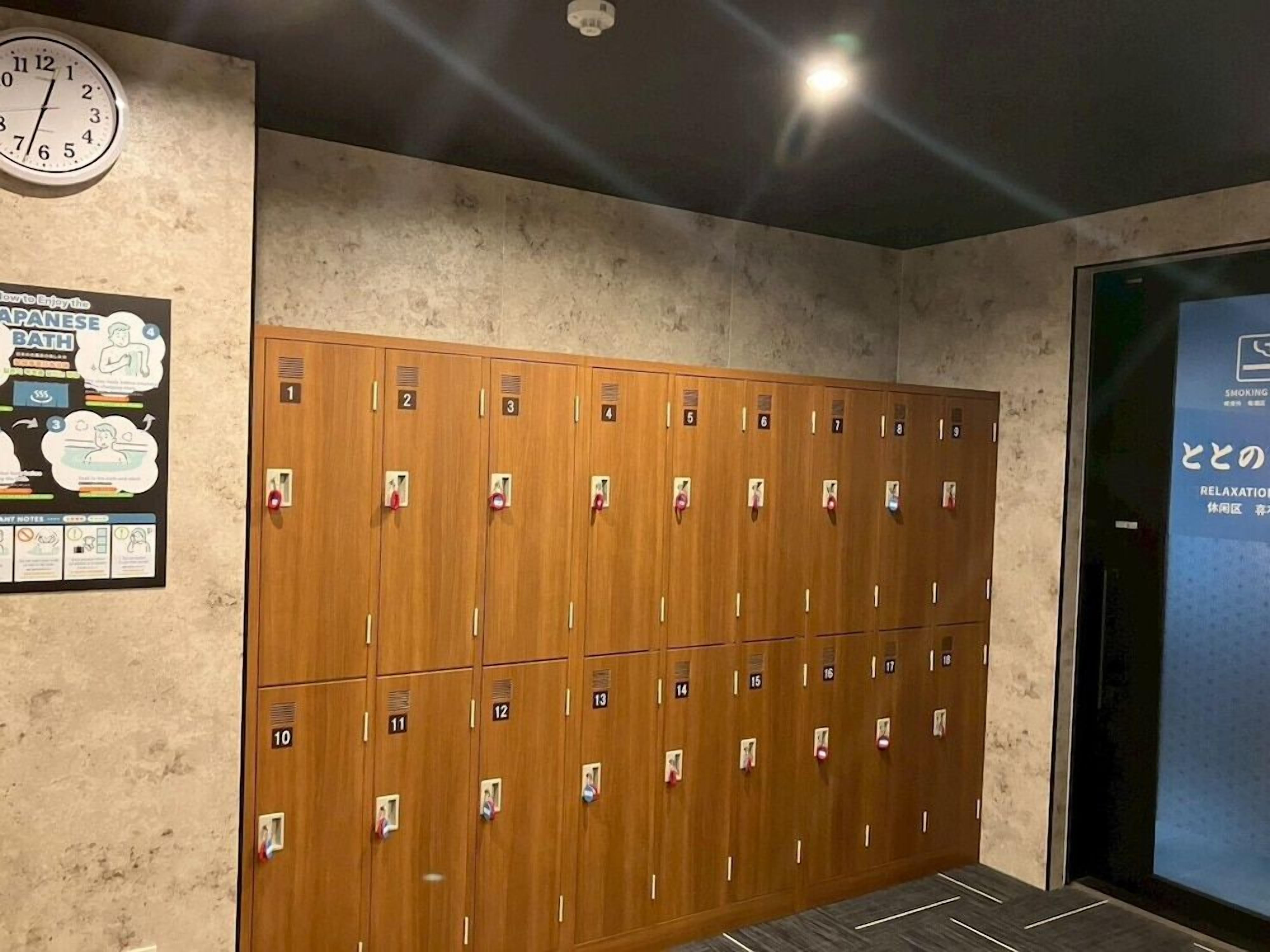 A row of wooden lockers with numbered compartments, a clock on the wall, and a poster advertising a Japanese bath.