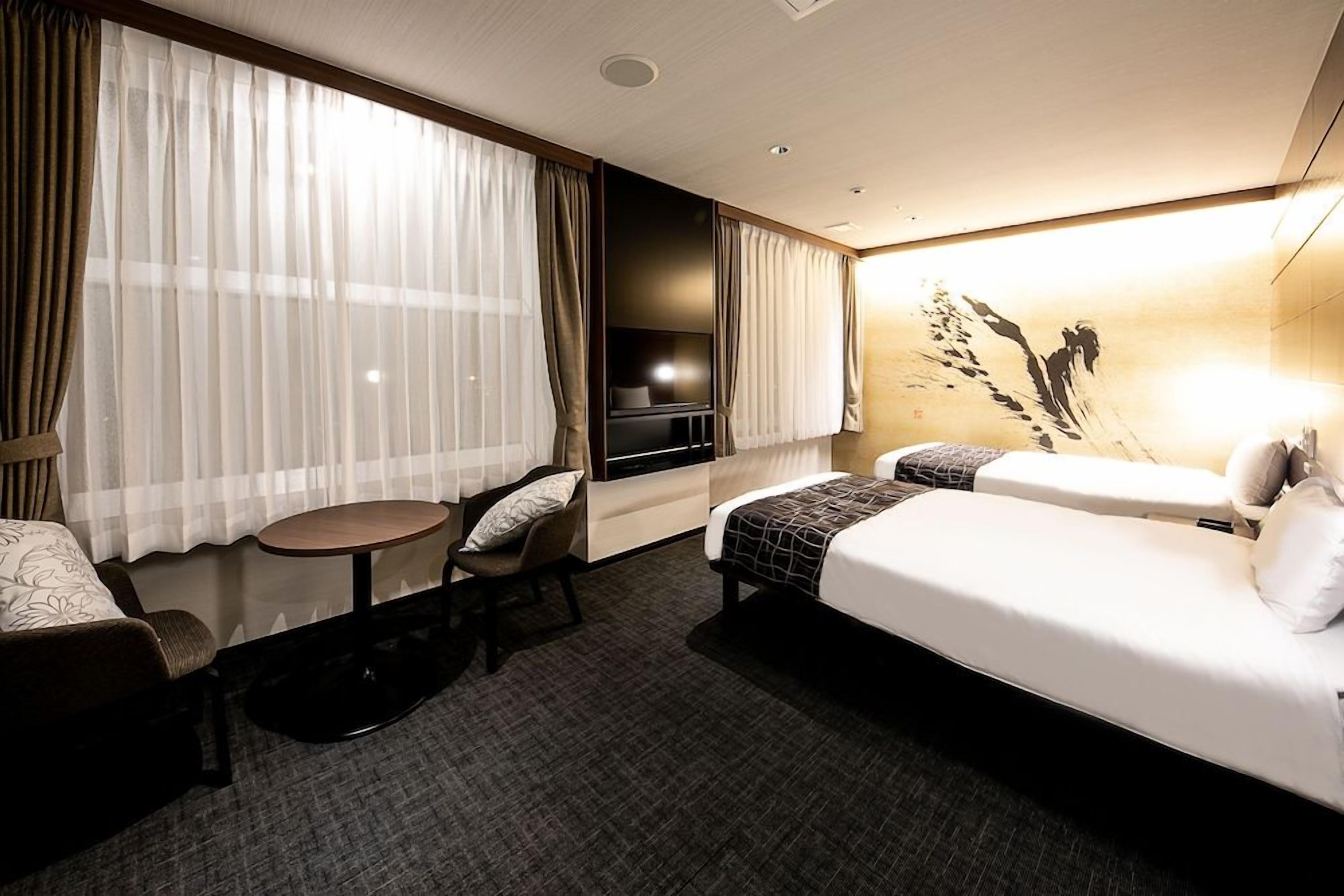 A hotel room with a bed, a desk, a chair, a TV, and a painting on the wall.