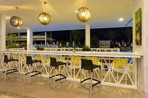 Uma área de bar com grades brancas, cadeiras pretas e luminárias pendentes.